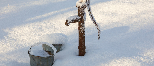 Pump vid en brunn som är täckt av snö och is sticker upp ur ett annars snötäckt landskap.