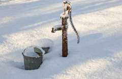 Pump vid en brunn som är täckt av snö och is sticker upp ur ett annars snötäckt landskap.