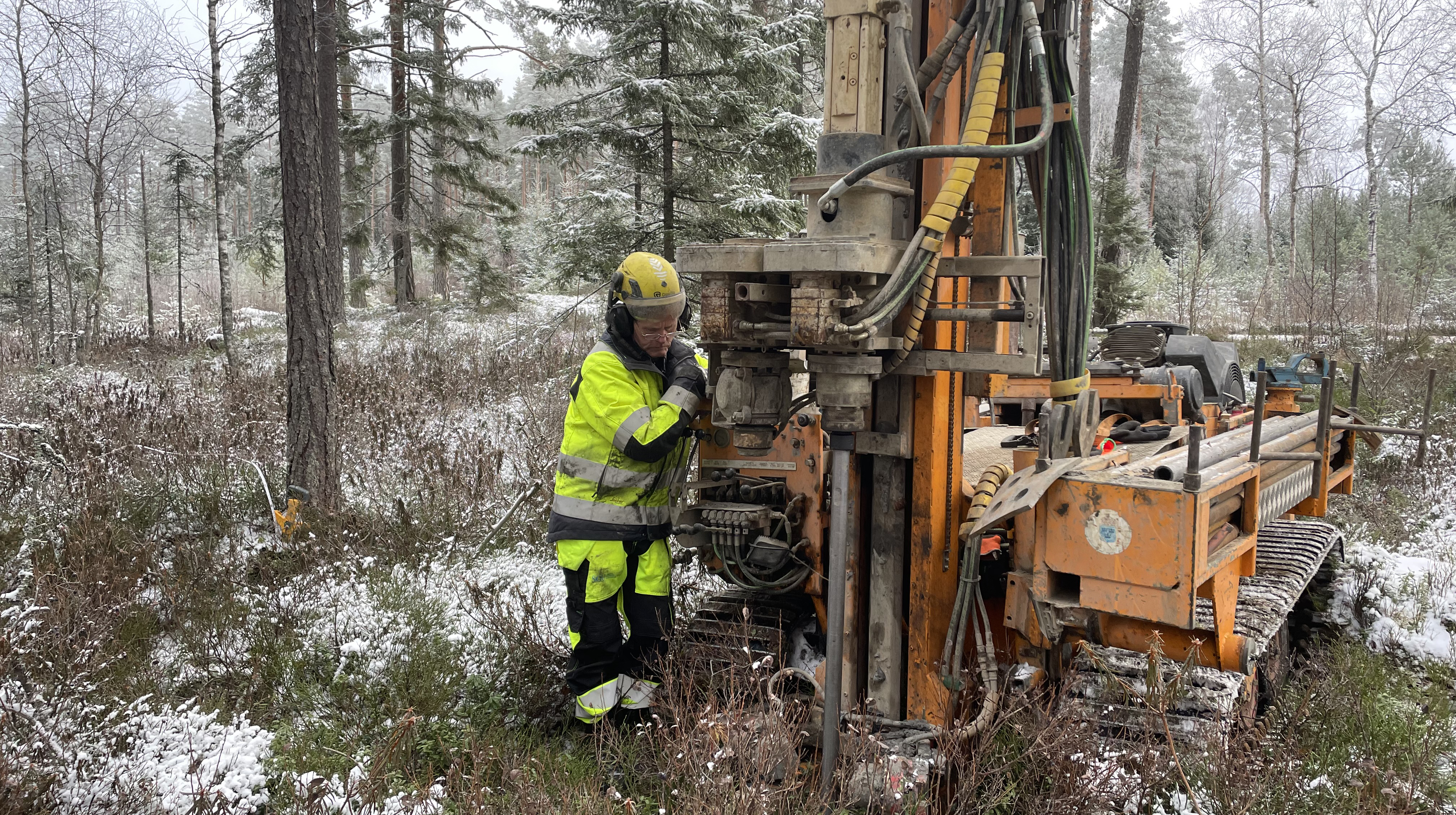 Person i skyddskläder vid en borrbandvagn i naturen.
