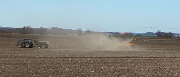 Traktor på åker som river upp moln av finkornigt material