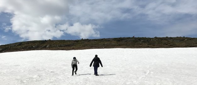 Två personer vandrar på ett snöklätt fjällområde. Foto.