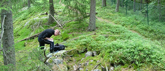 På bilden syns en person som står och antecknar. personen efinner sig i en skog.