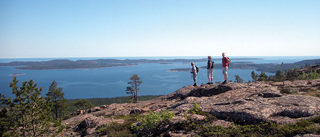 På bilden syns tre män med ryggsäcker. De står på ett berg och i bakgrunden syns vatten. På bilden syns tre män med ryggsäcker. De står på ett berg och i bakgrunden syns vatten.