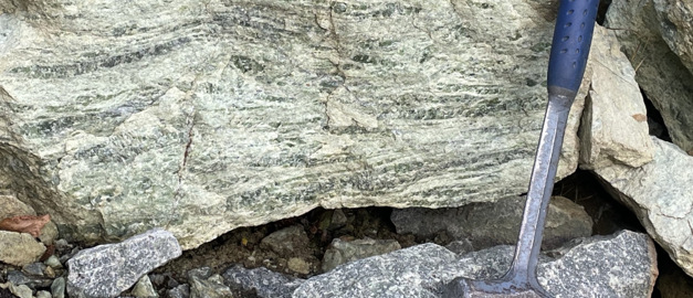 Sten med brottyta och en geologhammare