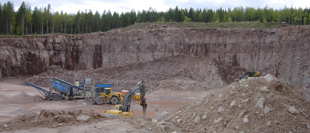 Bilden visar maskiner som arbetar i en bergtäkt tagen från kanten på täkten.