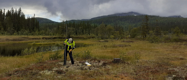 Person som står på en myr och tar jordprover med ett jordspett.