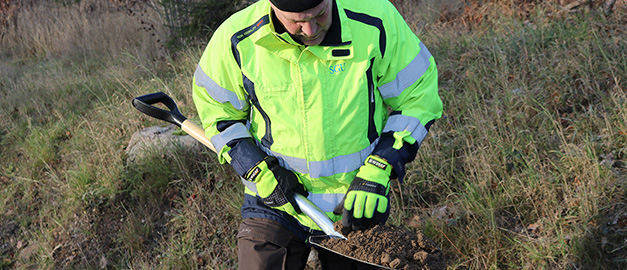 Foto av en man i varselklädsel som undersöker en spade med jord. Foto av en man i varselklädsel som undersöker en spade med jord.