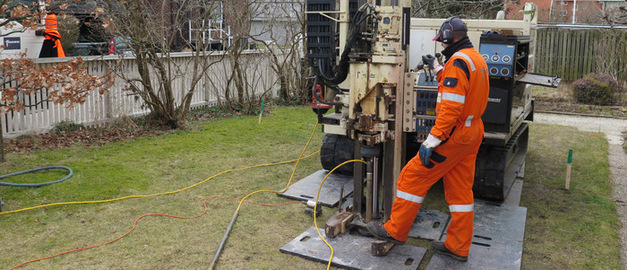 Två personer i varselkläder står vid en borr. Foto. Två personer i varselkläder står vid en borr. Foto.