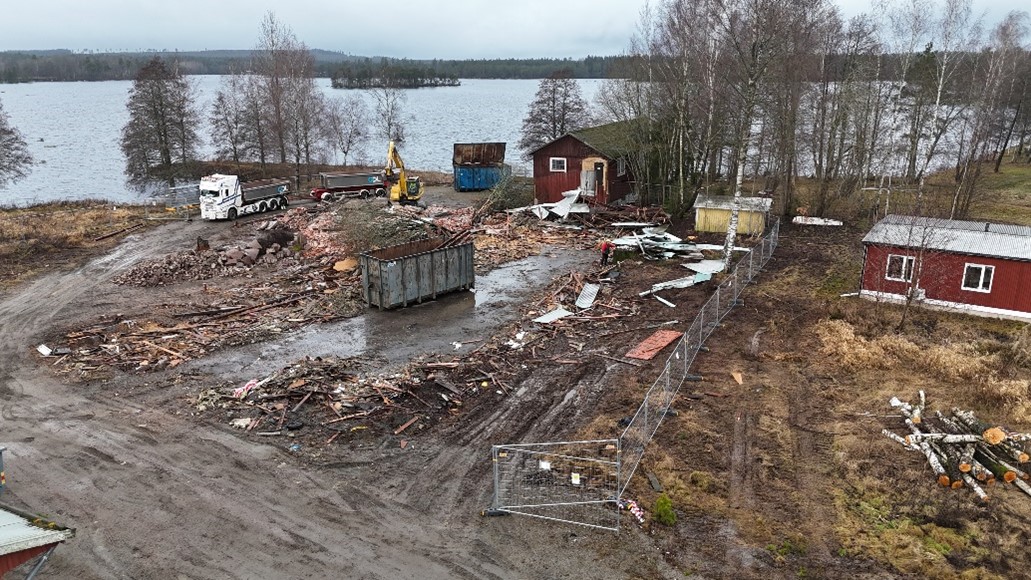 Bilden visar det pågående rivningsarbetet av Hjortsberga sågverk ovanifrån. På den leriga marken syns rester från byggnaden och maskiner som arbetar.